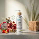 A bottle of Biotaderm Core Balanced Everyday Moisturiser with a wooden pump is displayed beside pomegranate, dragon fruit, rose hips, seaweed, and a small wooden box on a light surface. Infused with nourishing plant oils, this body moisturiser is formulated to promote balanced skin.