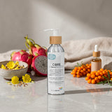 A bottle of Biotaderm Core Dry Sensitive Everyday Moisturiser on a stone surface with dragon fruit, sea buckthorn, yellow flowers, and a dropper bottle in the background—specially formulated with nourishing plant oils to deeply hydrate dry sensitive skin, making it an ideal body moisturiser.