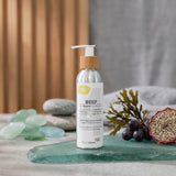 A bottle of Biotaderm Deep Oily Rich Moisturiser rests on a glass surface surrounded by stones, seaweed, and a halved passionfruit, emphasizing its nourishing plant oil blend that delivers deep hydration for oily skin without clogging pores.