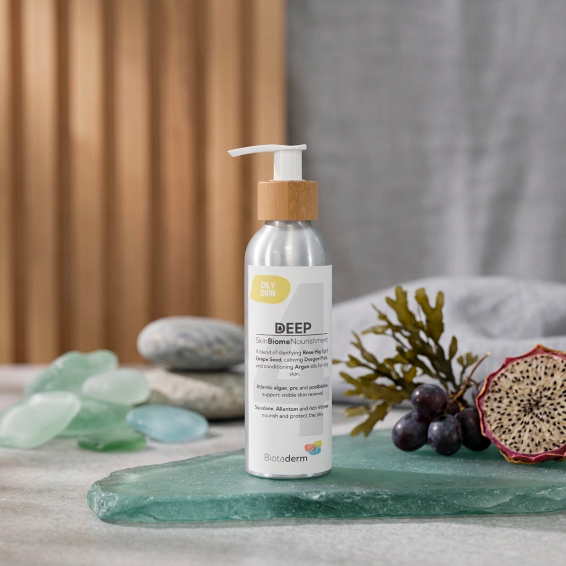 A bottle of Biotaderm Deep Oily Rich Moisturiser rests on a glass surface surrounded by stones, seaweed, and a halved passionfruit, emphasizing its nourishing plant oil blend that delivers deep hydration for oily skin without clogging pores.