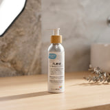 A silver bottle of Biotaderm Flow Balanced Light Moisturiser with a pump top sits on a wooden surface with a blurred background, promising balanced skin through its infusion of nourishing plant oils.